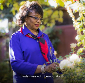 Linda, who lives with hemophilia B Linda, who lives with hemophilia B, standing in a flower garden and looking at a rose